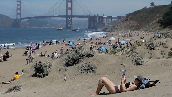 Sara Stewart, foreground, reads a book while away from crowds visiting Baker Beach during the coronavirus outbreak in San Francisco yesterday. Pic: AP