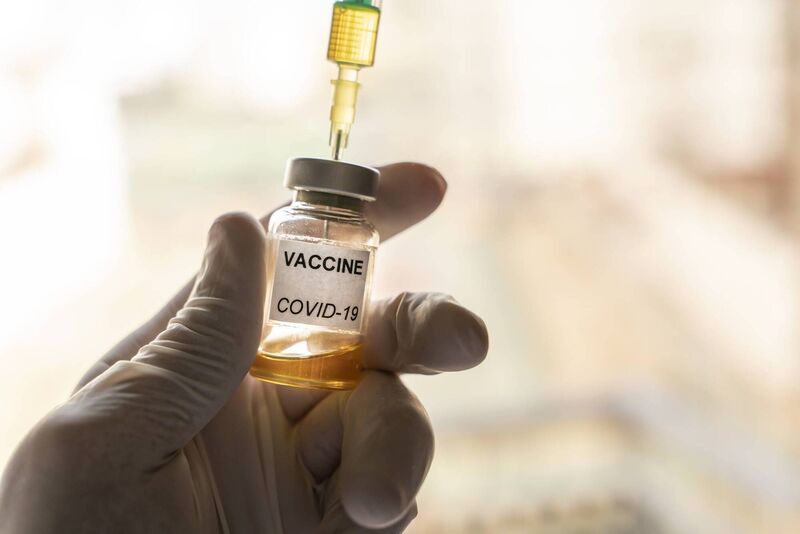 Cropped hand wearing a nitrile glove holding a Covid-19 vaccine vial and a syringe Cropped hand wearing a nitrile glove holding a Covid-19 vaccine vial and a syringe
