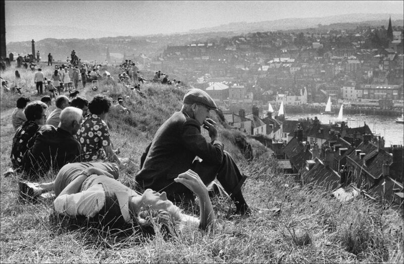 People out for a Sunday stroll sit and enjoy the view of the bay with its yachts and the town perched on the hillsides. Whitby, Yorkshire, UK. 1974. Photo: Ian Berry / Magnum Photos People out for a Sunday stroll sit and enjoy the view of the bay with its yachts and the town perched on the hillsides. Whitby, Yorkshire, UK. 1974. Photo: Ian Berry / Magnum Photos