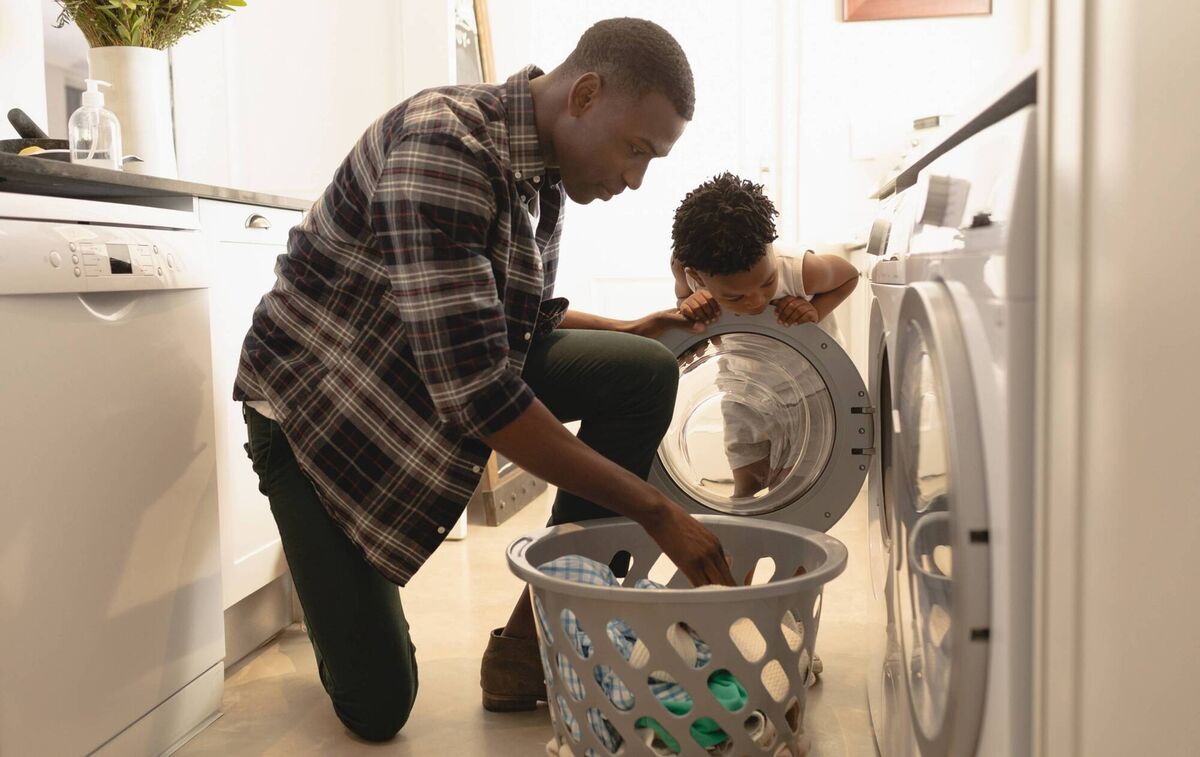 A father and son putting washing in the machine. PA