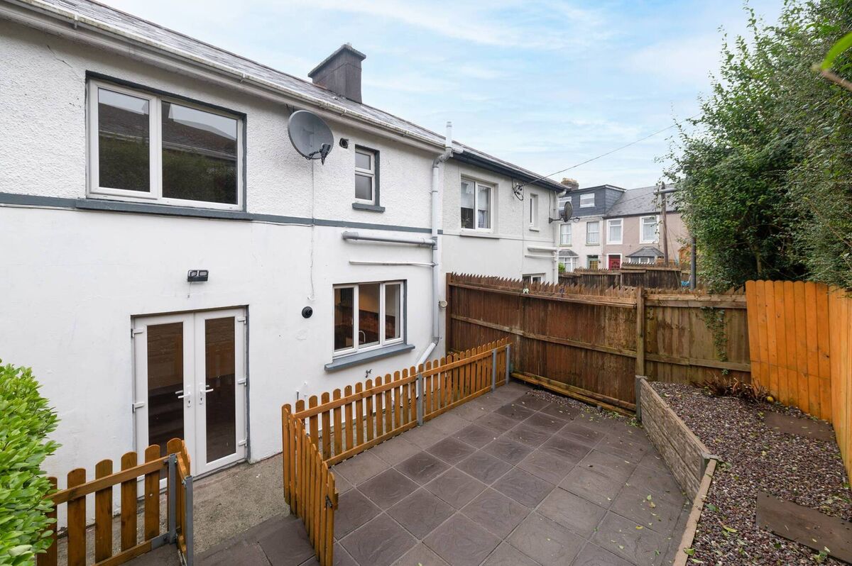 The raised patio at the rear sheltered by fencing and trees.