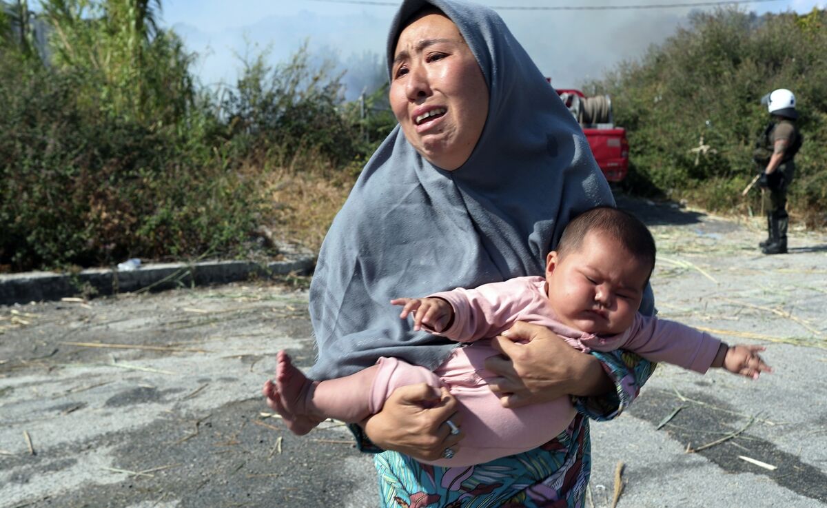 A woman holds her baby as she runs to avoid a small fire in a field near Mytilene town, on Lesbos. Thousands of asylum-seekers had to sleep in the open after successive fires destroyed the notoriously overcrowded Moria camp in September 2020. Picture: AP /Petros Giannakouris