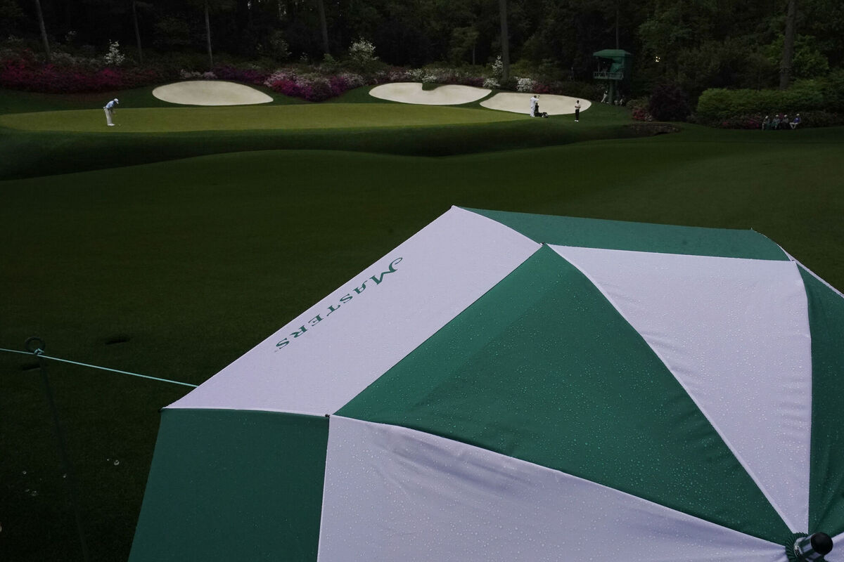 A spectator uses an umbrella against the rain while Will Zalatoris putts on the 13th hole during the third round of the Masters golf tournament on Saturday, April 10, 2021, in Augusta, Ga. (AP Photo/Charlie Riedel)