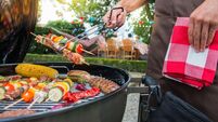Man grilling meat on garden barbecue party, in the background friends eating and drinking