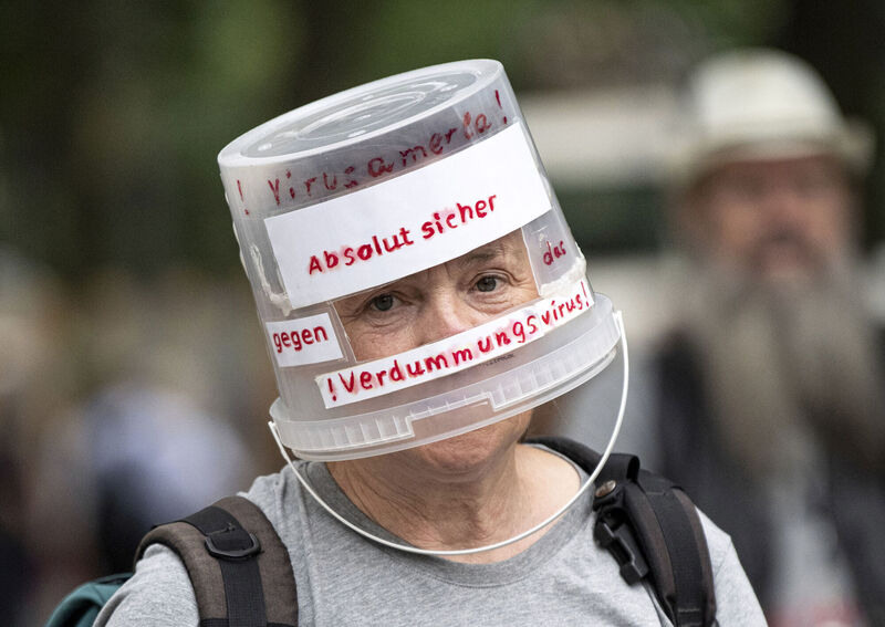 A demonstrator walks through Berlin-Charlottenburg with a plastic bucket placed on his head reading 'Absolutely safe against the stupidity virus', in Berlin last Sunday. Governments must listen carefully, understand people’s anxieties, and identify actual and potential protest leaders before they engage, debate, or try to convince the public of some crazed conspiracy theory. Photo: Fabian Sommer/dpa via AP
