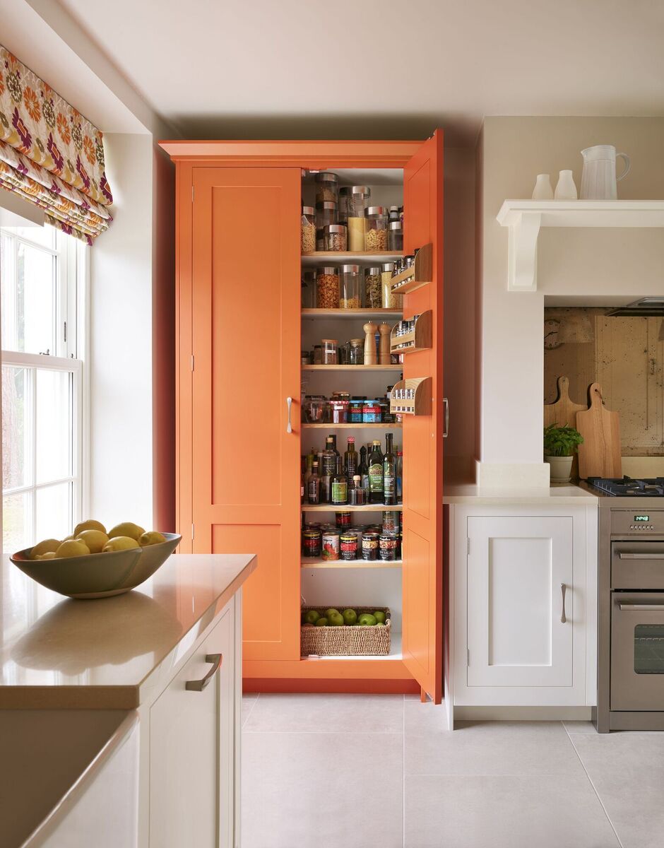 A dream two-door (linen press style) larder cupboard in spicey orange sits in the recess of a traditional country kitchen holding cans and long storage style condiments. For perishable foodstuffs, choose a cooler, darker situation, Harvey Jones (UK).