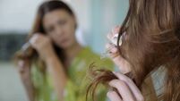 Hair care. Woman applying oil on hair ends in the bathroom in front of the mirror. Split hair tips, dry hair or sun protection c