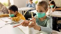 Elementary student wearing protective face mask and disinfecting her hands in the classroom.