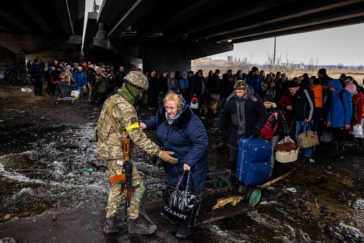 A Ukrainian serviceman helps evacuees gathered under a destroyed bridge, as they flee the city of Irpin, northwest of Kyiv, on March 7, 2022. Picture: Dimitar Dilkoff, AFP