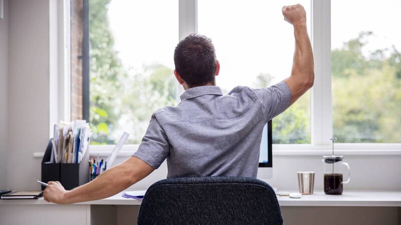 Rear View Of Man Working From Home On Computer  In Home Office Stretching At Desk