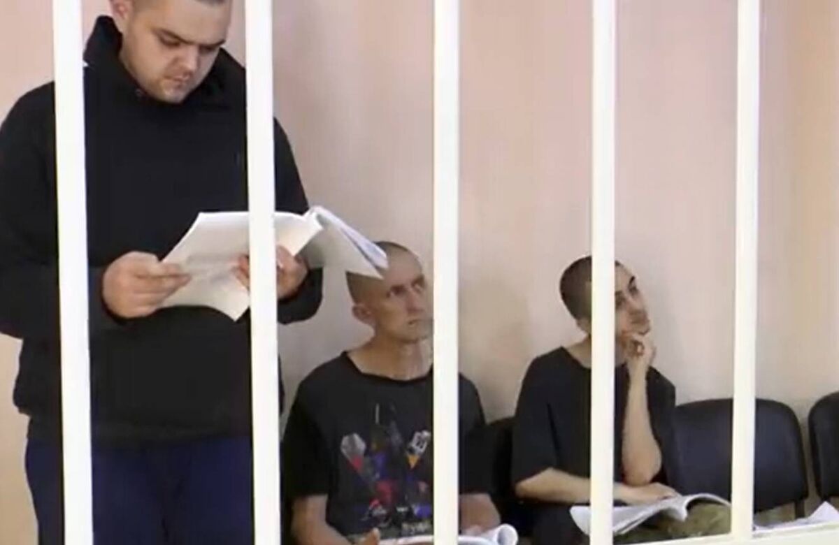 During the proceedings, the three men were held in a cage with black bars, guarded by soldiers. During the proceedings, the three men were held in a cage with black bars, guarded by soldiers.