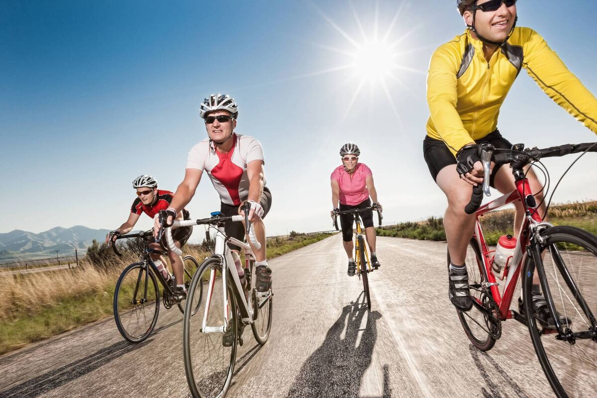 A small group of four road cyclists rides down an empty rural road with the sun at their backs for exercise and fun.