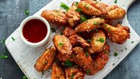 Baked chicken wings with sesame seeds and sweet chili sauce on white wooden board.