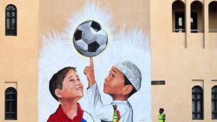 <p>DREAM FACTORY: A worker pushes a wheelbarrow past a mural in Doha</p>