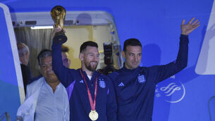 Argentina’s Lionel Messi holds the World Cup trophy as he leaves the plane (Gustavo Garello/AP)