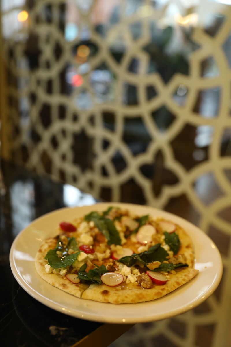 Nan panir Sabi is a flat but fluffy nan bread topped with feta cheese, chopped walnuts, thinly sliced radish, mint leaves, and then drizzled with honey