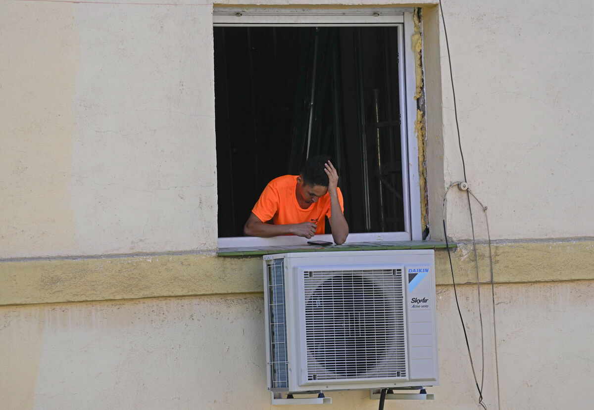A worker looks at his phone during a break by a newly installed air conditioner unit. Picture: AP Photo/Paul White
