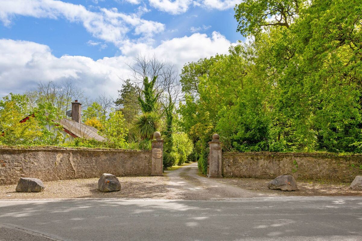 Low-key entrance and start of the property's long water-fronting approach avenue with gate lodge on left