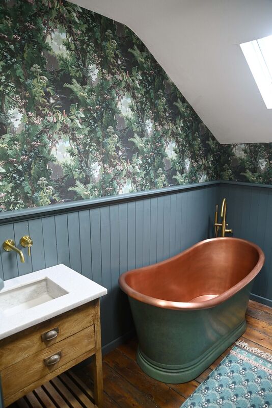 The starring role is given to an extra-deep copper bathtub, surrounded by forest-themed wallpaper.