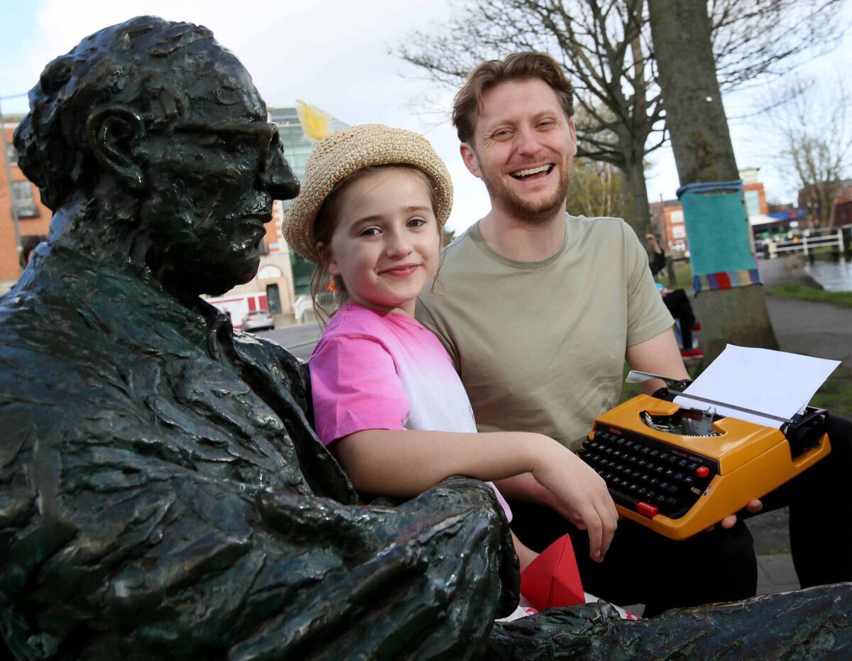 Seven-year-old Ruby Byrne and poet Stephen Maguire pose with the statue of Patrick Kavanagh, celebrating Poetry Day Ireland.