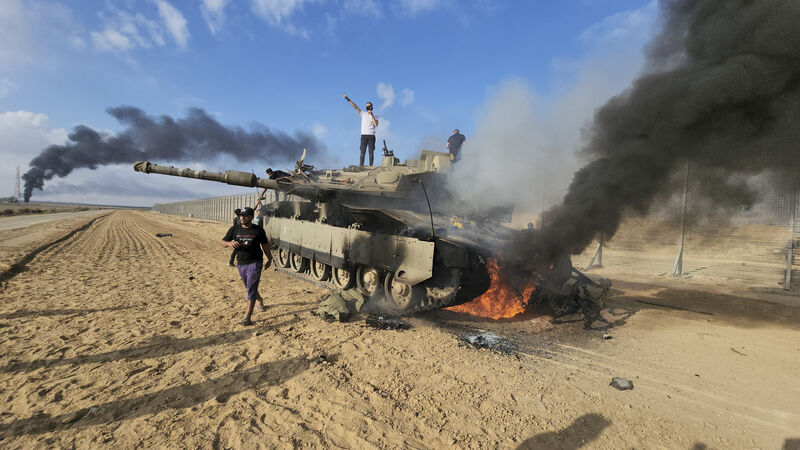 Palestinians celebrate by a destroyed Israeli tank at the Gaza Strip fence (Hassan Eslaiah/AP)