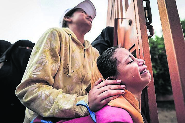 People mourn as they stand behind a metal fence near the bodies of victims who were killed in Israeli bombardment before their burial, outside the morgue at Nasser hospital in Khan Yunis in the southern Gaza Strip on November 14, 2023 