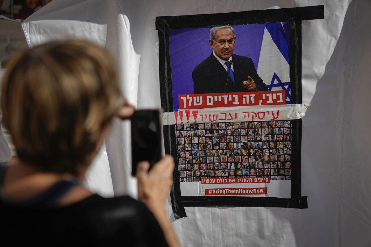 A woman takes a photo of a poster showing Israelis held captive in Gaza plastered underneath a picture of Benjamin Netanyahu in Tel Aviv. Picture: AP Photo/Ariel Schalit
