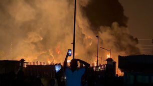 Residents watch a plume of smoke from a burning oil depot in Conakry, Guinea (AP)