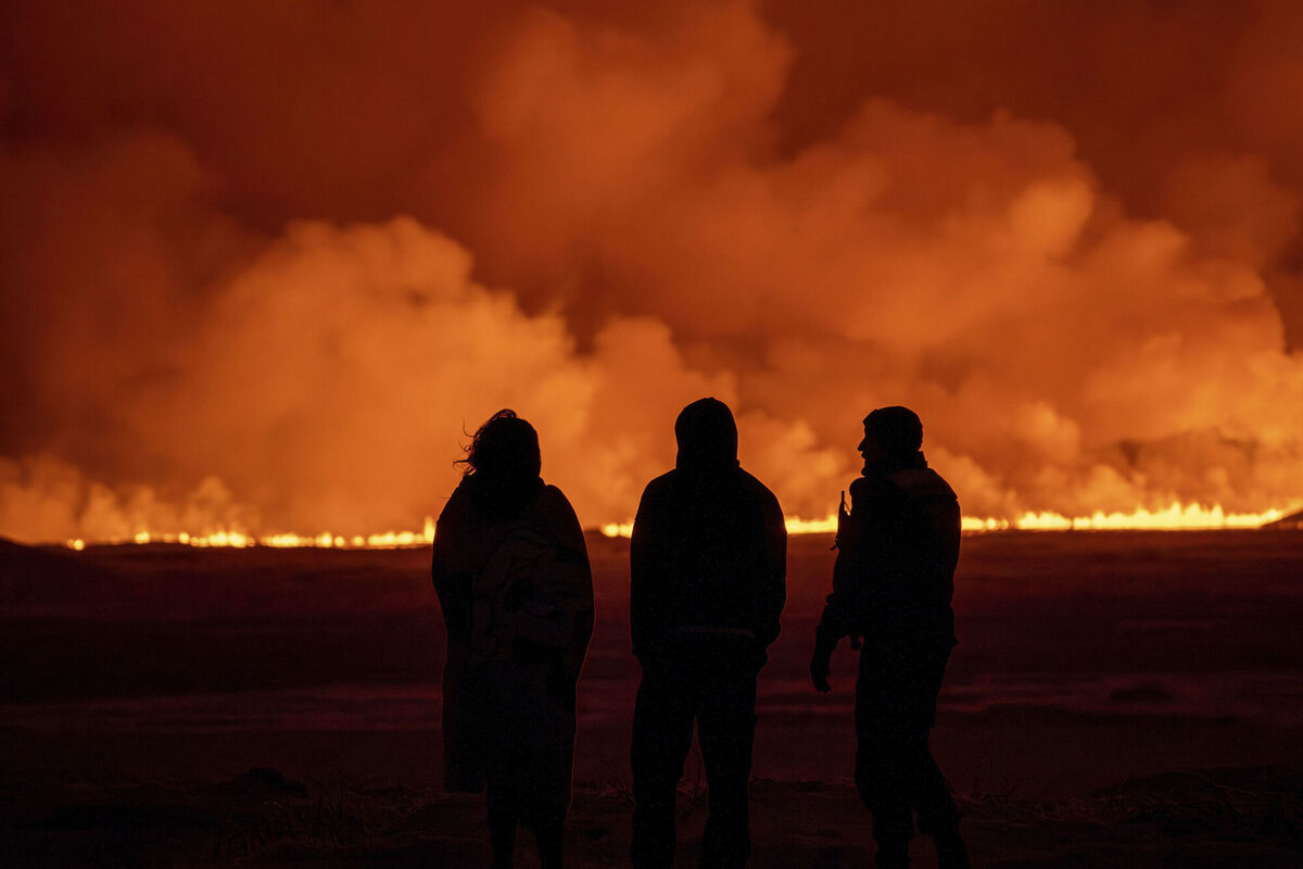 People watch as the night sky is illuminated caused by the eruption of a volcano on the Reykjanes Peninsula. Picture: AP Photo/Brynjar Gunnarsson