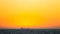 A cargo ship is seen at a the horizon amidst the golden sky.