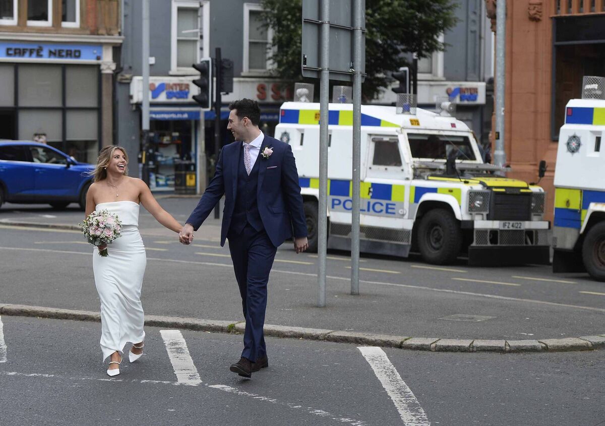 A newly married couple cross the road as PSNI officers line the streets as two protests are scheduled to take place in Belfast city centre. 
