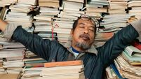 Lecturer reading a book in the university library, looking exhausted and tired from studying. Sleeping on stacks of books.