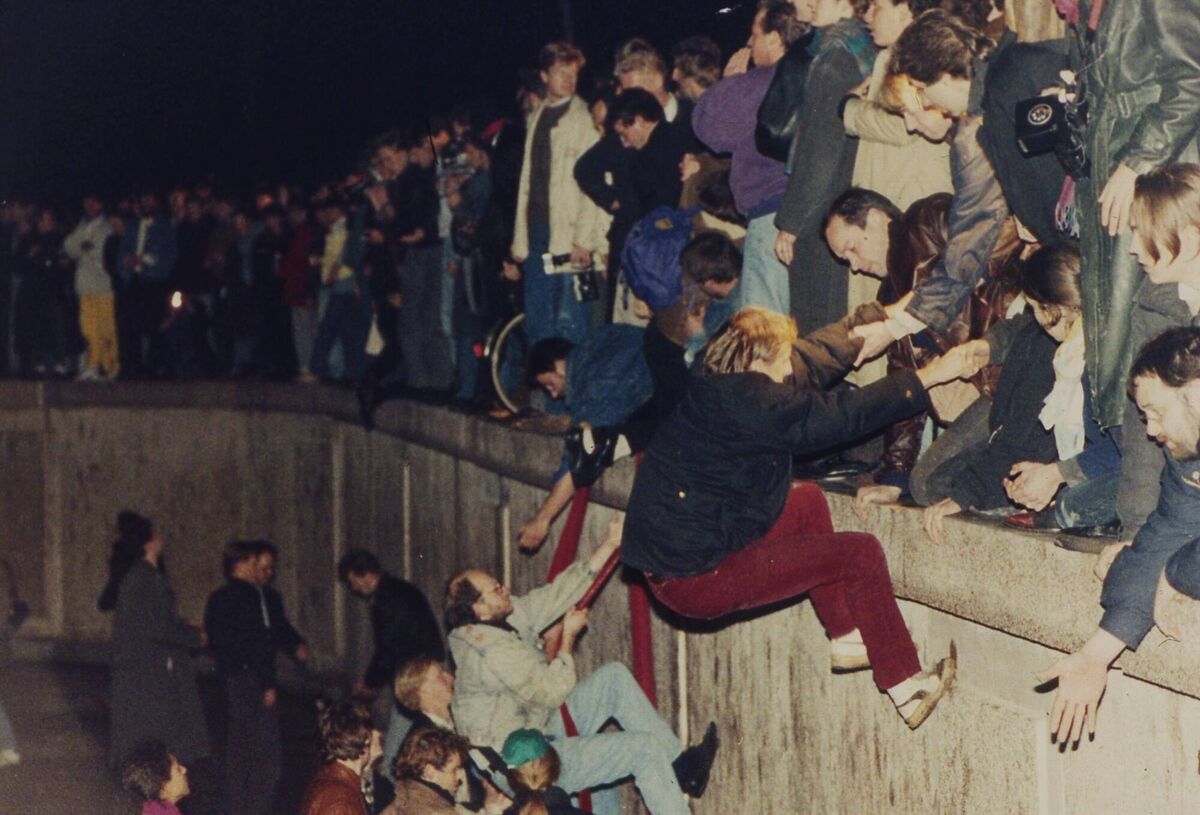  East Berliners getting helping hands from West Berliners as they climb the Berlin Wall.