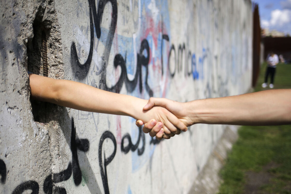 Tow tourists from France shake hands through a hole in the remains of the Berlin Wall at the Berlin Wall memorial at Bernauer Strasse in Berlin.