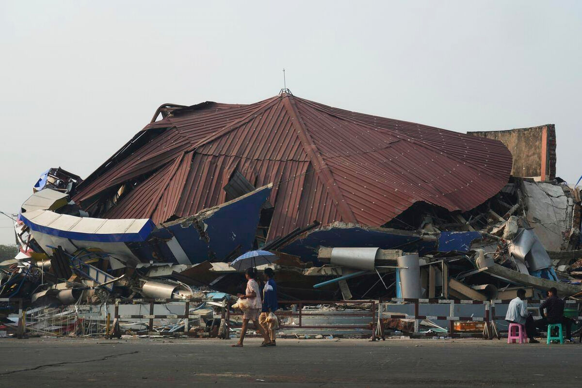 People sit by while others walk past a collapsed building in Naypyitaw, Myanmar, Saturday, March 29, 2025, after an earthquake has rocked Myanmar on Friday. (AP Photo/Aung Shine Oo)