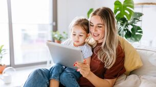 <p>Mother and daughter using a digital tablet together. They are sitting on the sofa at home. The daughter is sitting on his mothers lap. Very hapy and smiling. Close up with Tight crop</p>