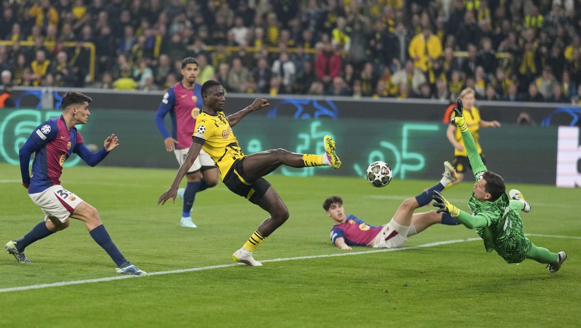 Barcelona's goalkeeper Wojciech Szczesny, right, blocks a shot by Dortmund's Serhou Guirassy, center, during the Champions League quarterfinals second leg soccer match between Borussia Dortmund and Barcelona, at the Signa-Iduna Park in Dortmund, Germany, Tuesday, April 15, 2025. (AP Photo/Matthias Schrader)