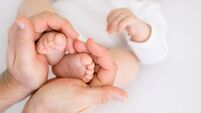 The father holds the tiny legs of a newborn baby in his palms.