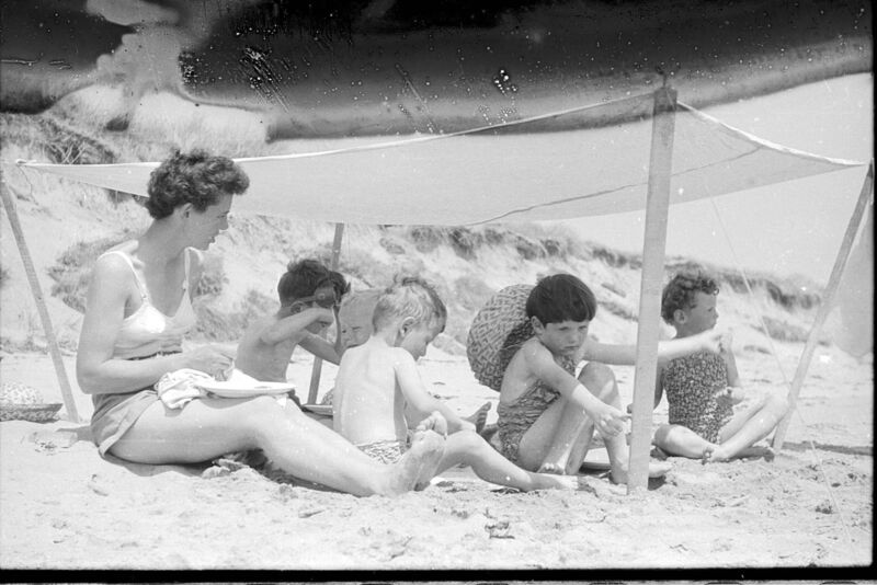 A woman shades children on the beach. 