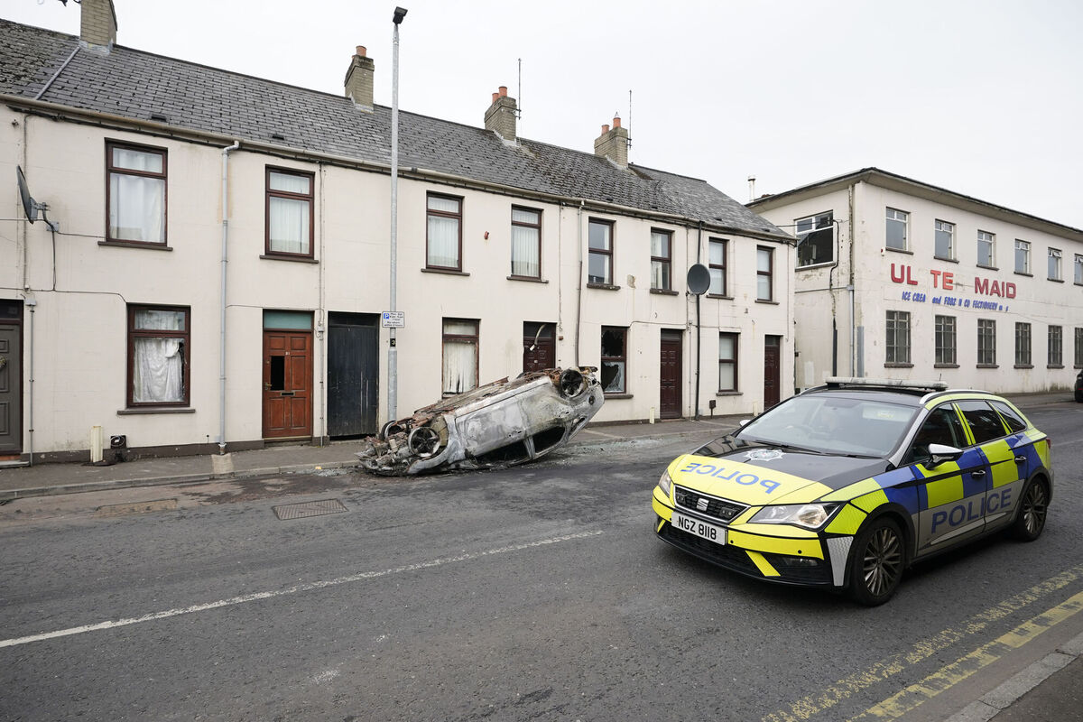 A police car drives past a burnt-out overturned car on the street following a second night of violence in Ballymena, during a protest over an alleged sexual assault in the Co Antrim town. Picture: Niall Carson/PA Wire