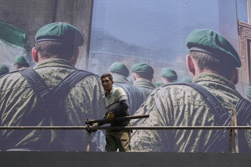 A worker stands in front of an anti-Israeli banner depicting Iranian soldiers heading to attack Israeli territory, at Islamic Revolution Square in Tehran, Iran, Saturday, June 14, 2025. (AP Photo/Vahid Salemi)