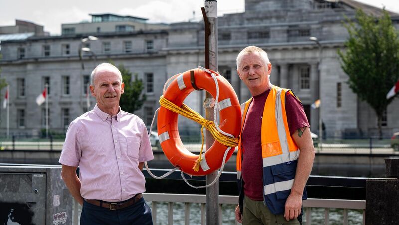 Colin Russell and Stephen Scully from Cork City Council’s Recreation Amenity Department pictured beside a lifebuoy station with Cork City Hall in the background.