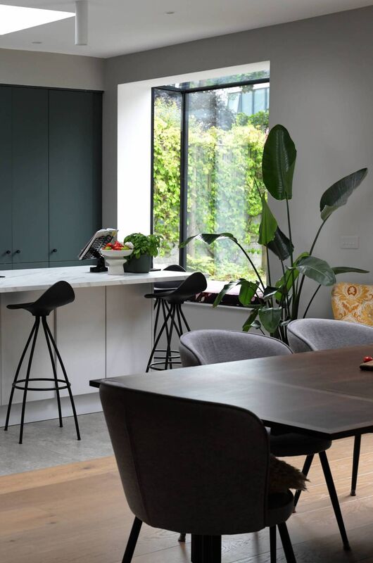 A view from the dining area to the kitchen with a large window seat and garden beyond.