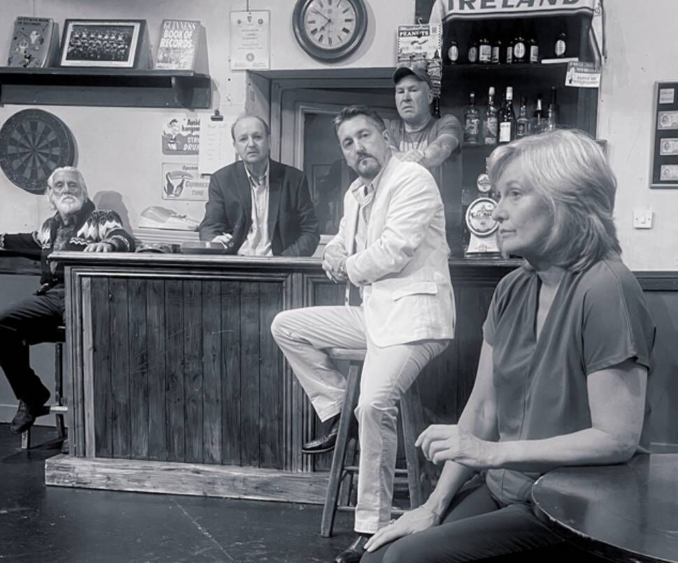 Kilmeen Drama Group production of The Weir. Denis O’Mahony as Jack and Ger Minihane as Brendan. Seated outside the counter left to right Sean Ahern as Jim, Gearóid McCarthy as Finbarr and Nora Scannell as Valerie. Nora also directs the show.
