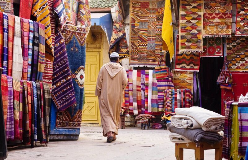 A local man in a djellaba passes carpet sellers in the market