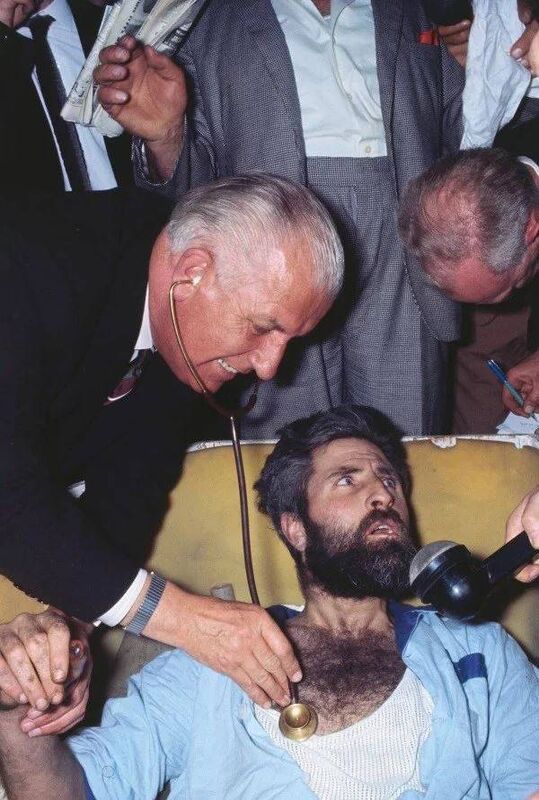 Mick Meaney conducting a media interview even as a doctor checks his health after his extraordinary feat of spending 61 days buried alive in London in 1968.