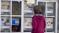 Woman looking at houses and flats in the window of an estate agent in London, UK