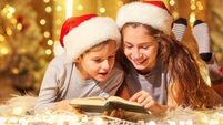 Two children on the floor read a book in a room  with Christmas