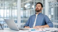 A pensive businessman sits at his desk with closed eyes, taking a moment for himself in a modern office.