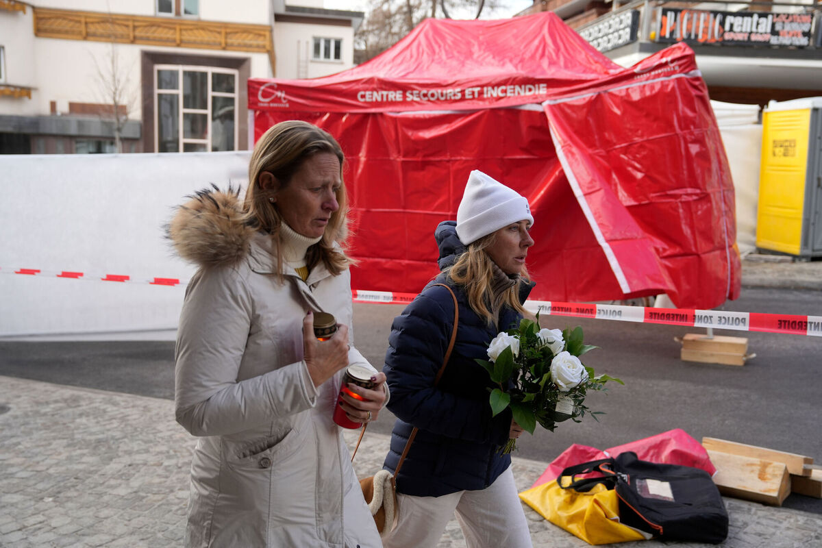 People gather to pay tribune near the sealed off Le Constellation bar, where a devastating fire left dead and injured during the New Year's celebrations in Crans-Montana, Swiss Alps, Switzerland, Friday, Jan. 2, 2026. (AP Photo/Baz Ratner)